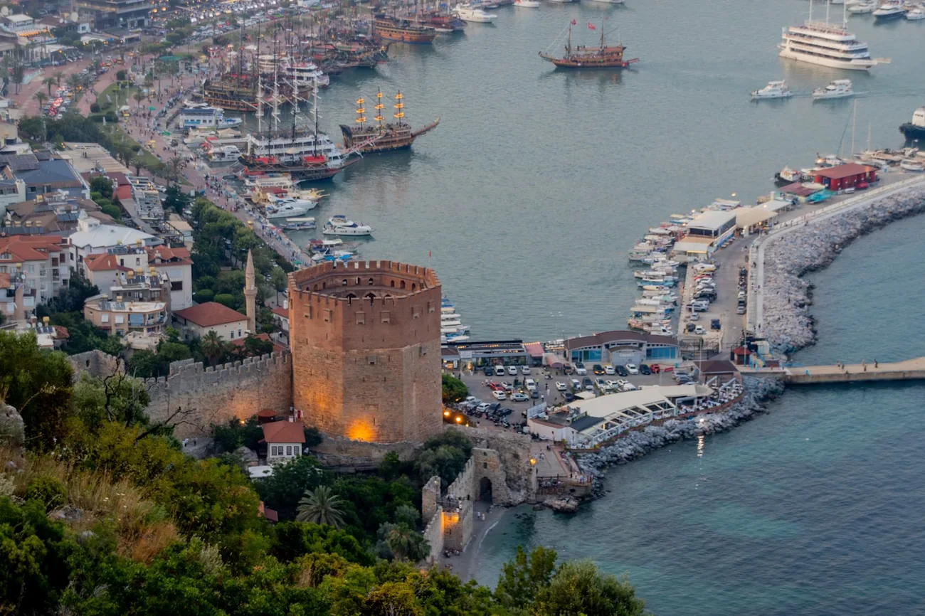 Det røde tårnet og havna i Alanya i skumringen, med utfluktsbåter ved kaia