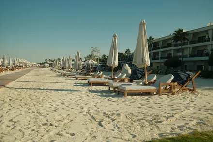Solsenger og hvite parasoller på en bred sandstrand foran et hotell