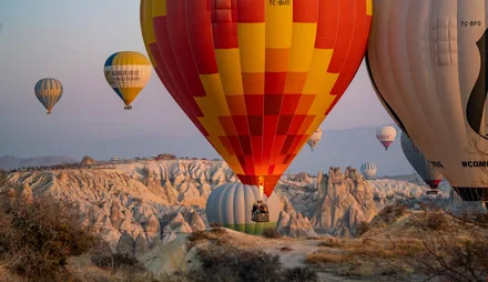 Fargerike luftballonger løfter seg over tuffklippene i Kappadokia i morgenlys