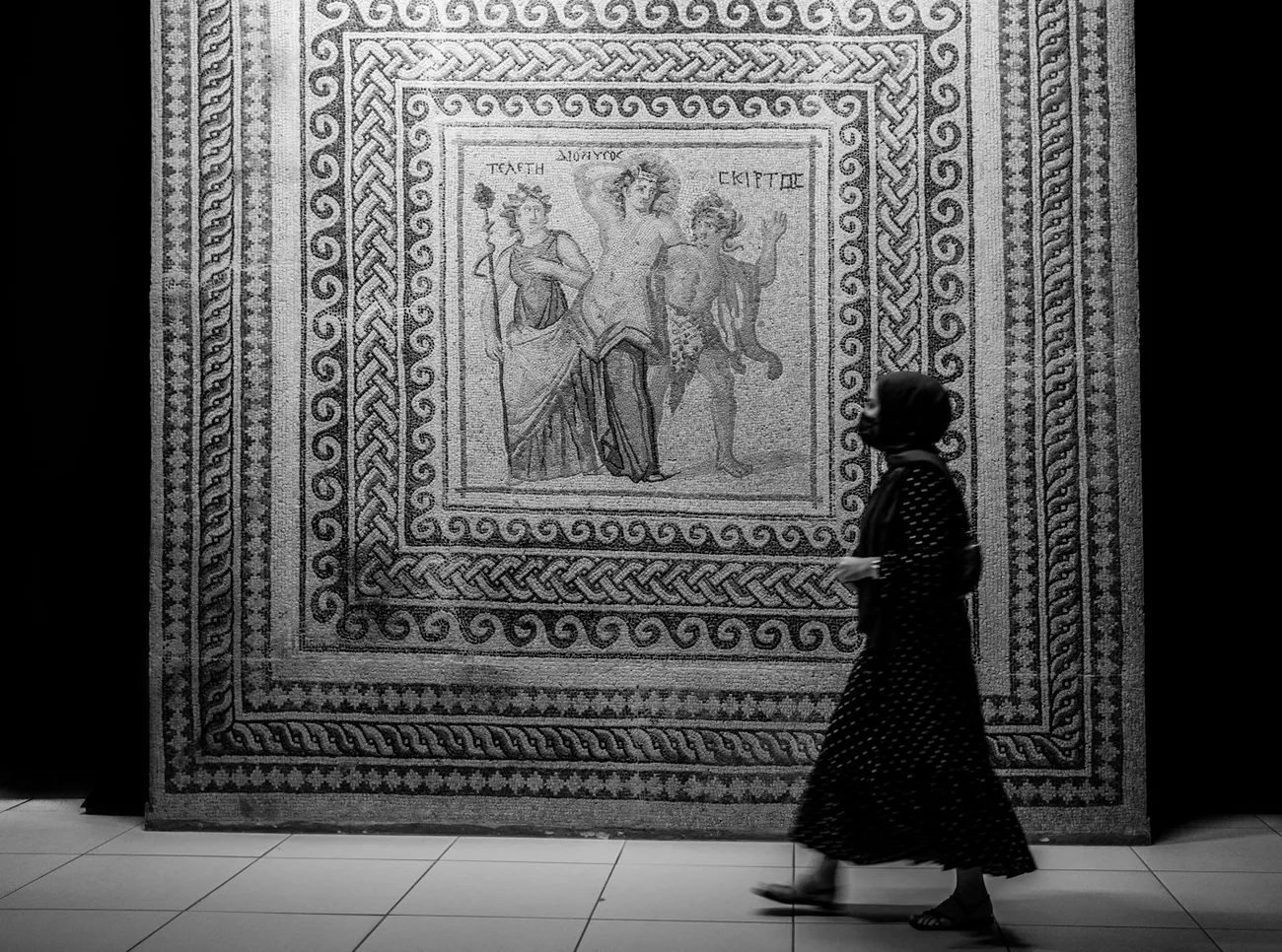 Kvinne går forbi en stor romersk mosaikk med gudefigurer i mosaikkmuseet