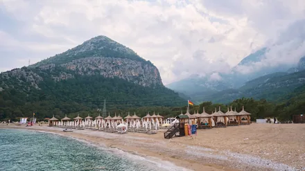Strand med solsenger og parasoller foran en skogkledd fjellside i Kemer