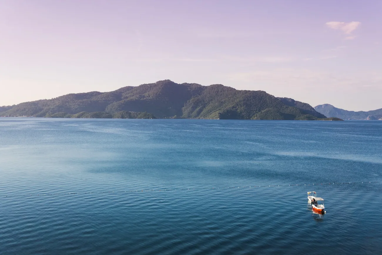Rolig blå bukt med en liten båt og grønnkledde åser ved Marmaris