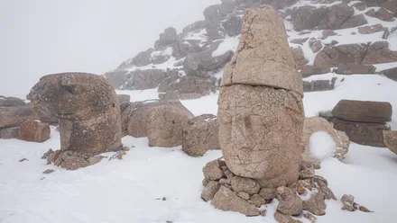 Et av de kolossale steinhodene på Nemrut Dağı i snø og tåke