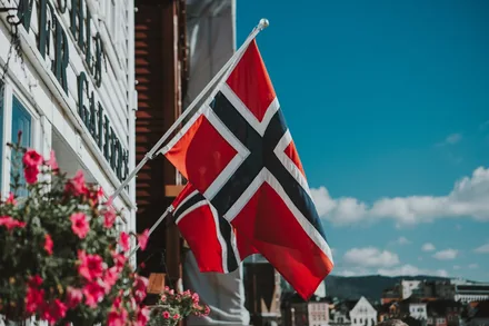 Norske flagg på flaggstenger utenfor en hvitmalt bygning mot blå sommerhimmel