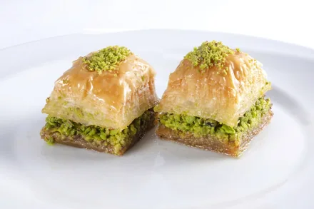 To biter baklava med sprø filodeig og grønn pistasj på hvit tallerken