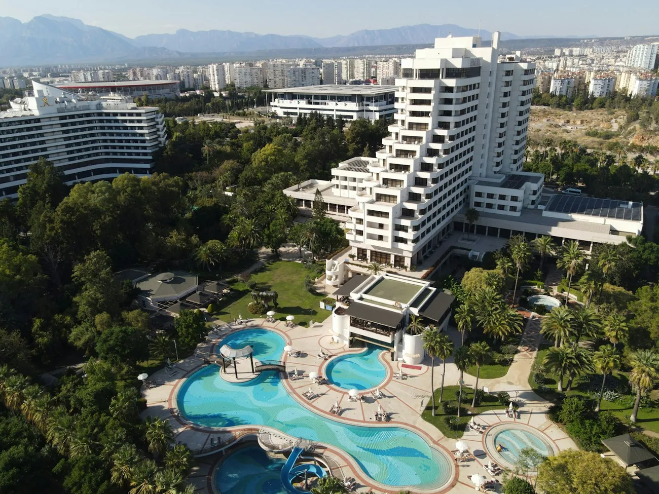 Et stort feriehotell i Antalya med svømmebasseng, palmer og fjell i bakgrunnen