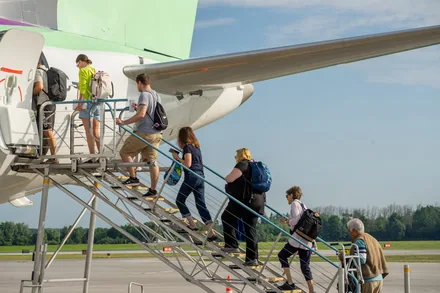 Reisende går om bord i et fly via flytrappen på en solrik dag