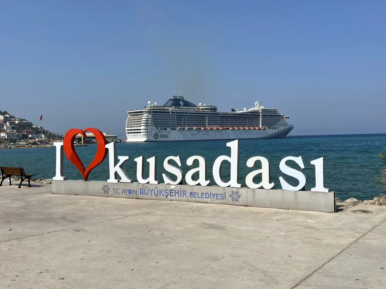 Et cruiseskip på reden utenfor Kuşadası, med byens skilt på kaia i forgrunnen
