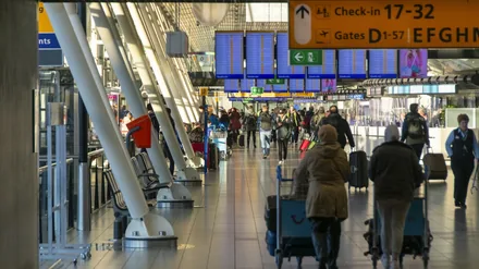 Reisende med koffert på vei gjennom avgangshallen under infoskjermer