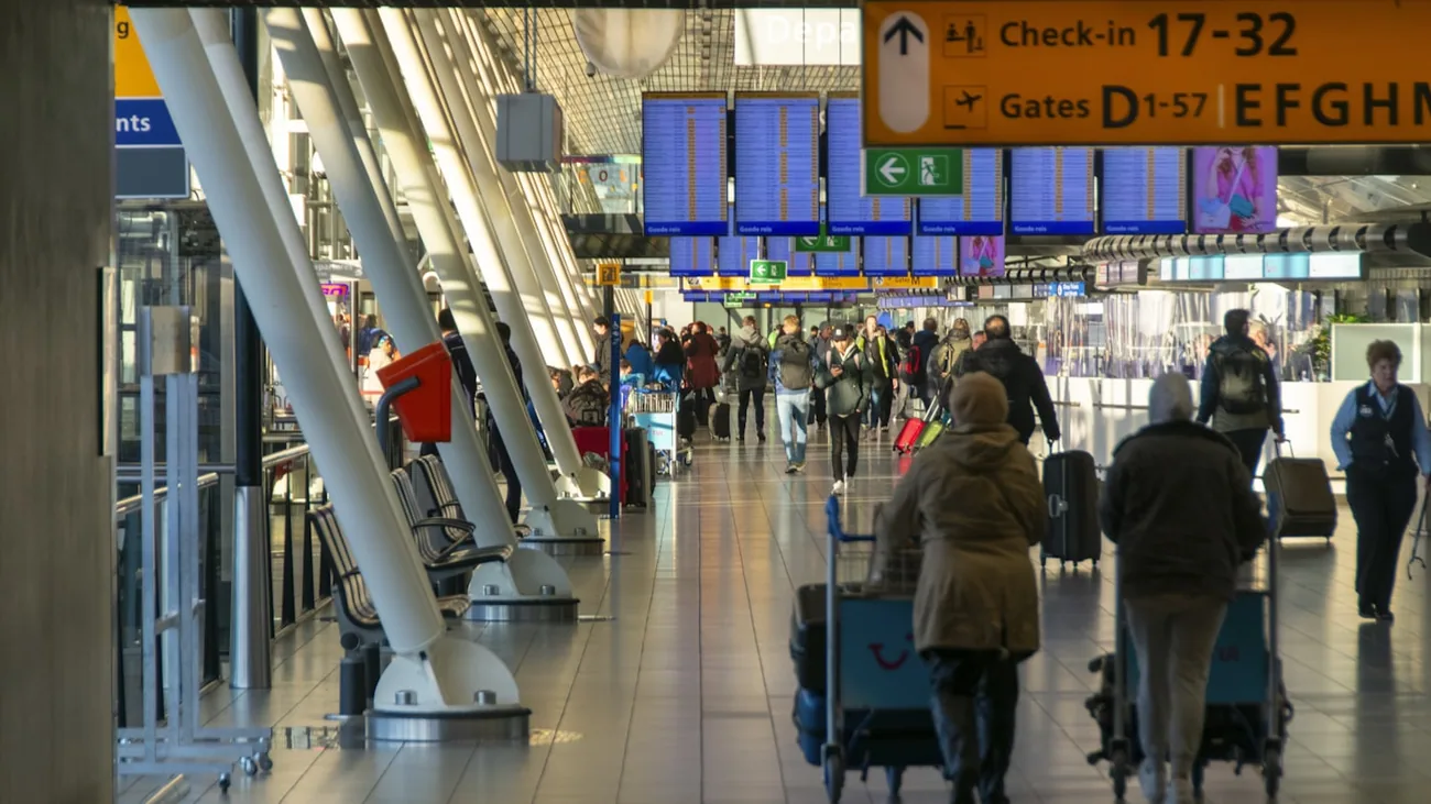 Reisende med koffert på vei gjennom avgangshallen under infoskjermer