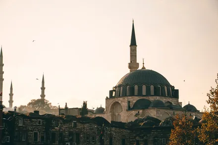 En osmansk moské med blygrå kuppel og slank minaret i motlys over takene i Istanbul