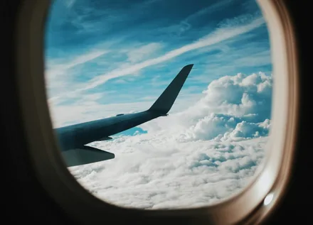 Utsikt gjennom det ovale flyvinduet mot vingen og skyene på turen
