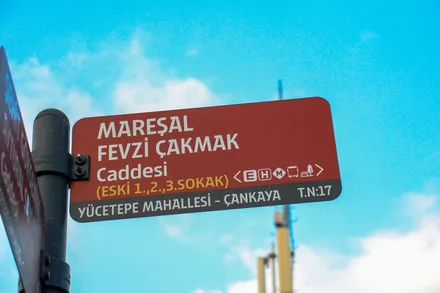 Et rødbrunt gateskilt i Ankara med tyrkiske bokstaver mot en blå himmel