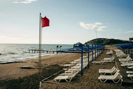 Rødt flagg på en tyrkisk strand med tomme solsenger